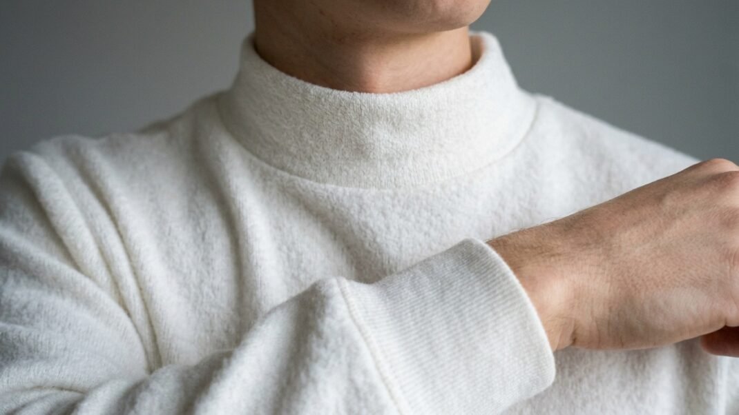 Close up view of the ribbed collar and textured fabric on a soft white long sleeve top.