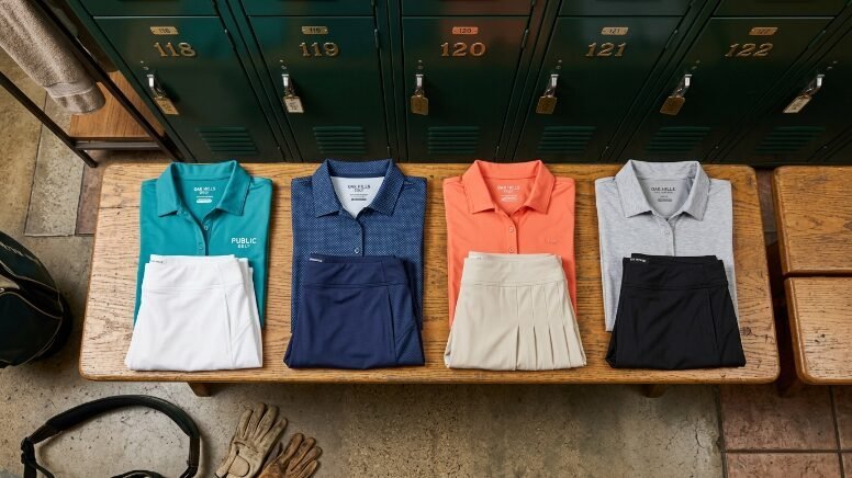 Top-down view of four folded golf polo shirts and matching pleated skorts arranged on a locker room bench.