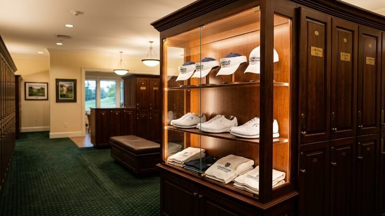 A glass display cabinet in a golf clubhouse filled with branded caps, white golf shoes, and folded white towels.
