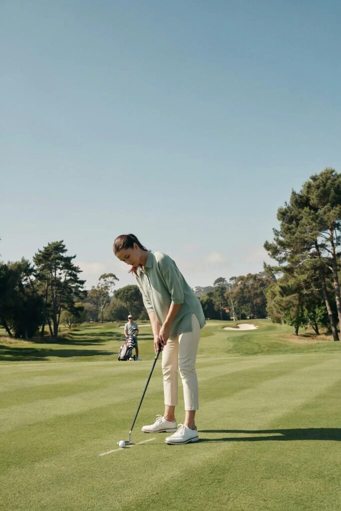 A woman wearing a winter hat and vest playing golf on a frosty field as birds fly by in the distance.