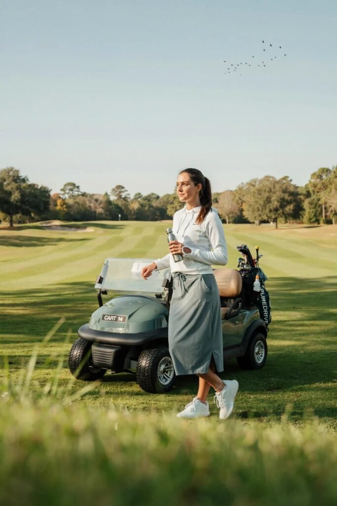 A woman in a black outfit crouches on a golf course to carefully set a white ball on the grass.