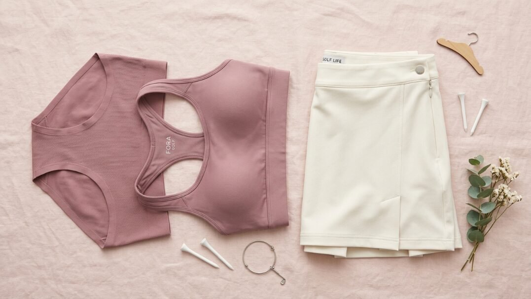 Flat lay of a mauve sports bra, matching underwear, and white skort with golf tees and a sprig of flowers.