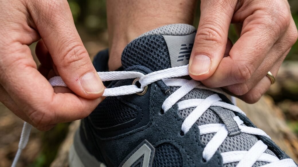 Close-up view of a person securing the laces on a dark navy and grey athletic shoe.