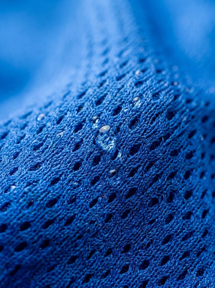 Close-up of moisture droplets trapped in the textured pores of a blue synthetic workout material.