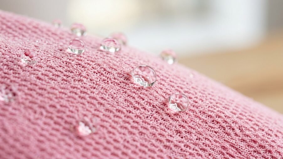 Close up of liquid spheres sitting on top of a soft woven rose colored textile surface.