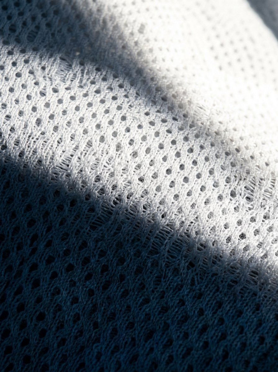 Detailed macro shot of white perforated textile showing sunlight casting a sharp diagonal shadow across the pattern.