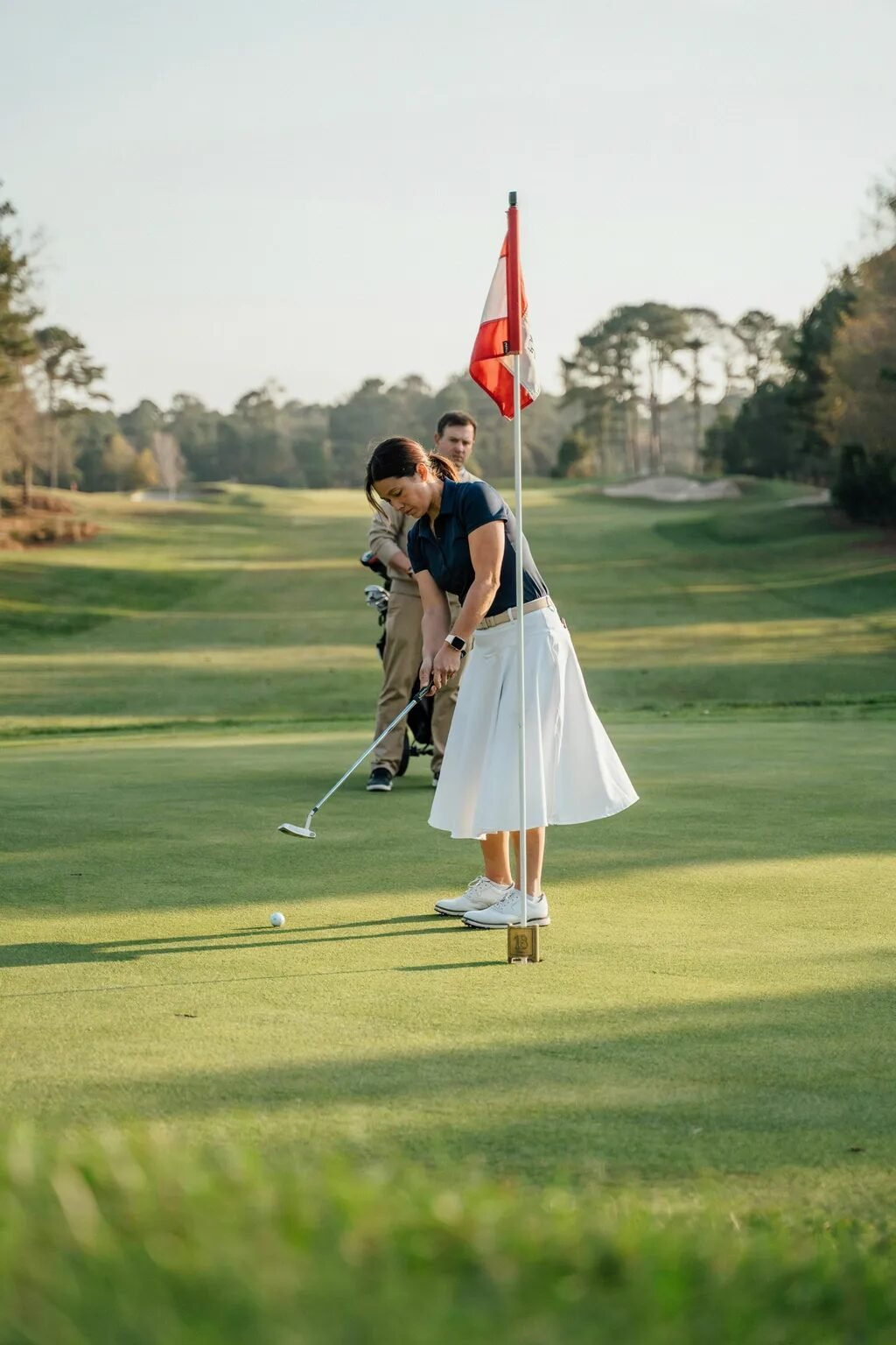 Golfer preparing to putt on the green while her partner observes from behind with a golf bag.