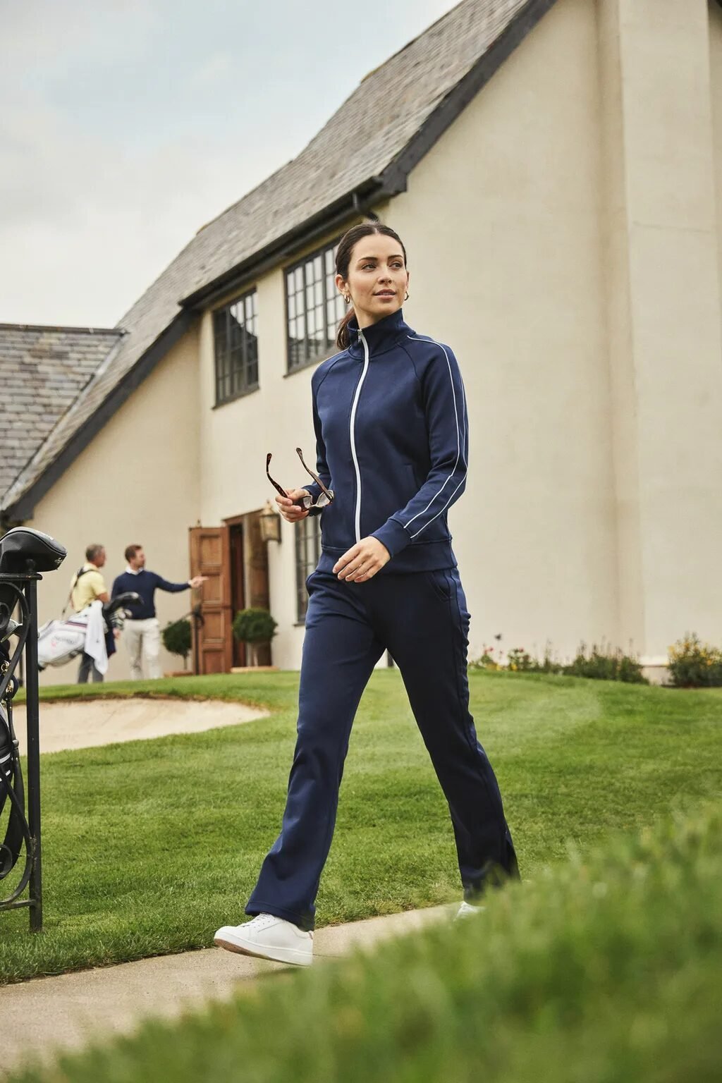 A woman in a navy athletic zip-up jacket and matching pants walking past a golf clubhouse.