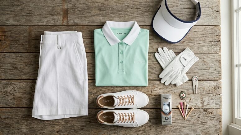 A mint polo shirt, white shorts, golf shoes, visor, and balls laid out on a rustic wooden table.